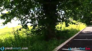 brunette casually sits in her car, lifting legs to display feet through black pantyhose outdoors